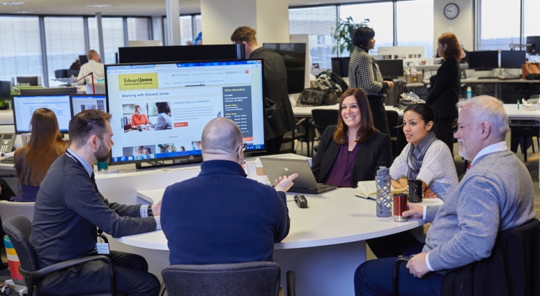 Group of associates seated around a conference table looking at a large-screen monitor