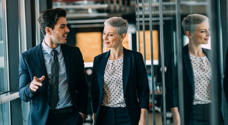 A man and woman walking down an office corridor.