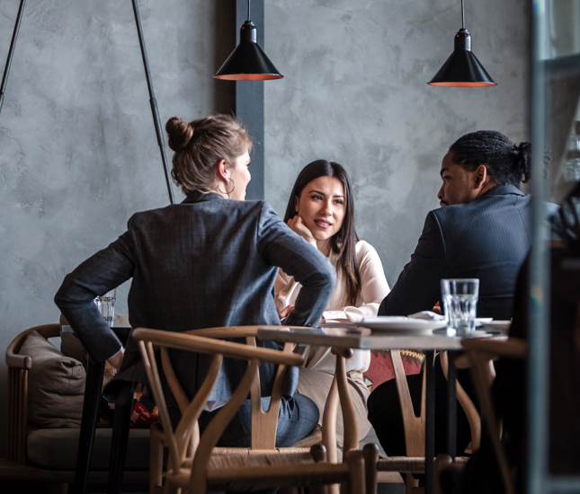 A man and two women seated around a table engaged in conversation.