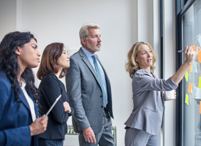 Three associates looking at Post-It Notes on a window while a fourth writes on a Post-It Note.