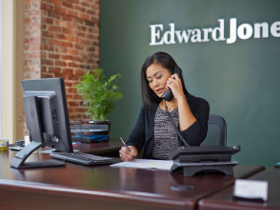 A woman seated at a desk with a telephone in one hand and a pen in the other hand.