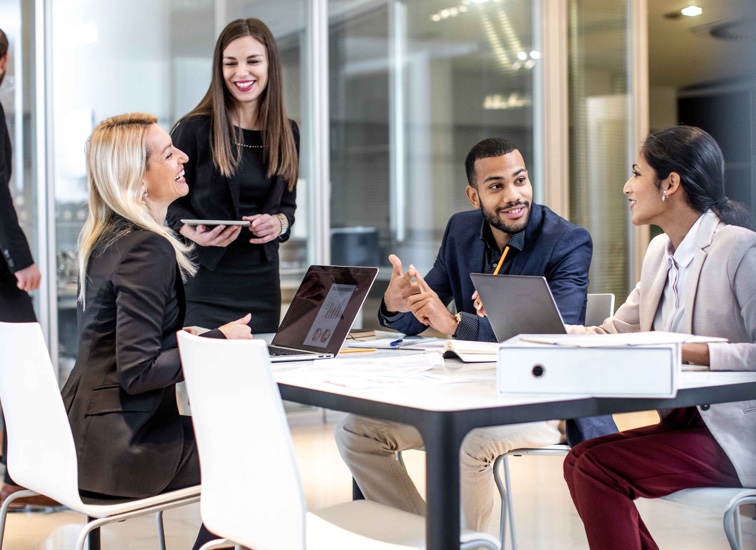 A group of smiling associates seated around a table having a conversation.